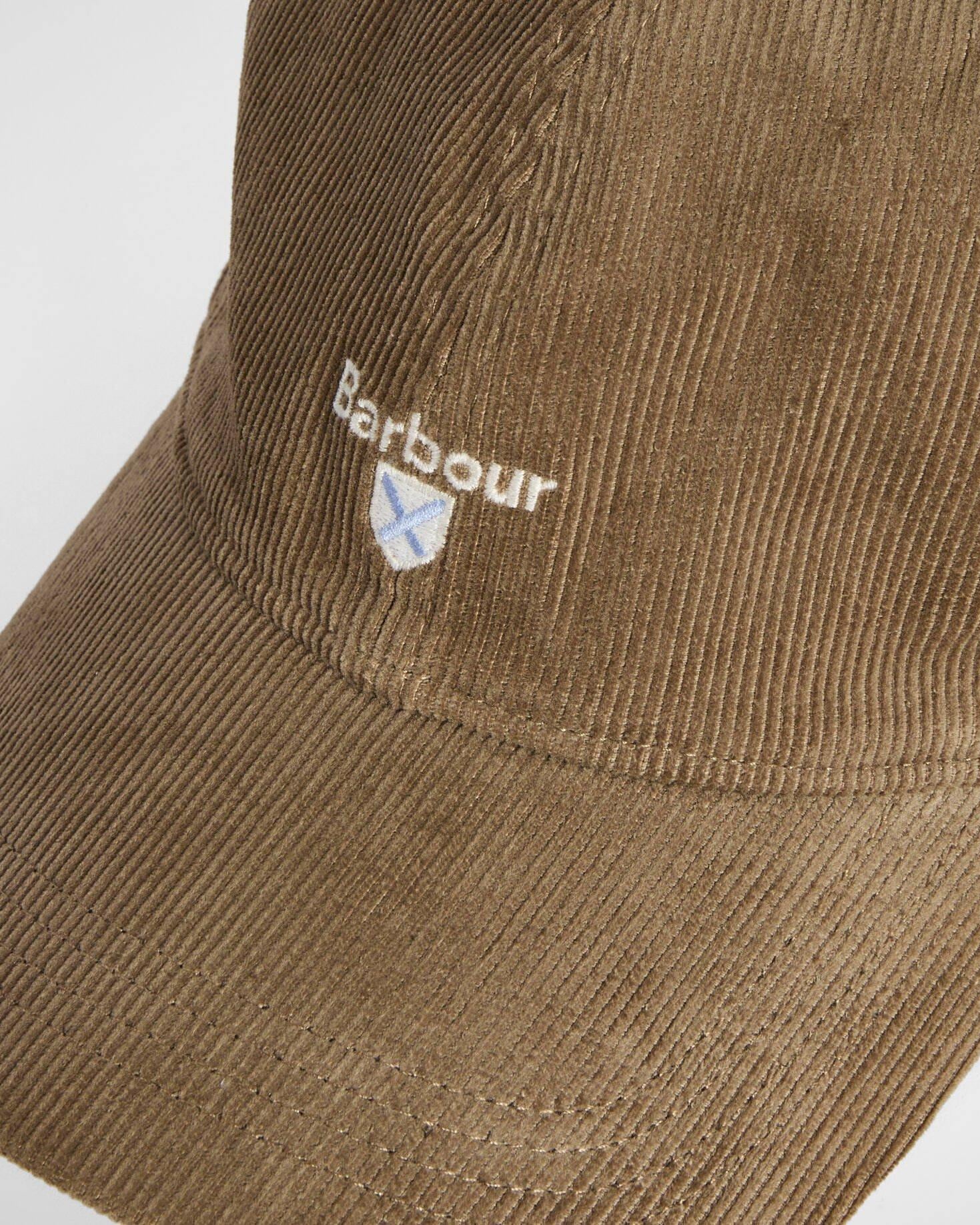 Nærbilde av Barbour caps. Ser struktur, logo med våpenskjold under. Plassering rett over brem